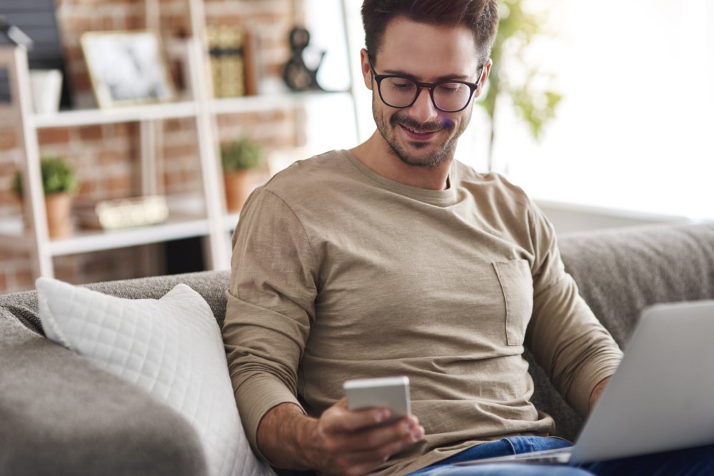 Ein mann som har PC-en sin i fanget medan han ser på telefonen sin.